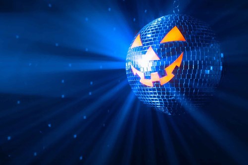 A disco ball styled like a glowing jack-o'-lantern, with orange eyes and a jagged smile, reflecting blue light in a dark party atmosphere
