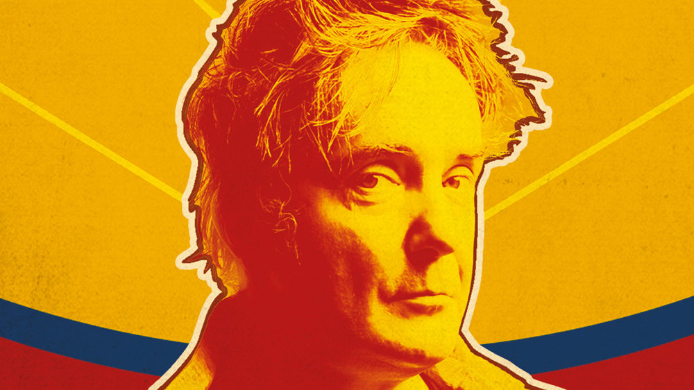 A bold, stylised portrait of a man in warm red and yellow tones, facing slightly to the side. The background features radiating yellow lines with a curved band of blue and red behind him, giving a vibrant, graphic poster-like feel.