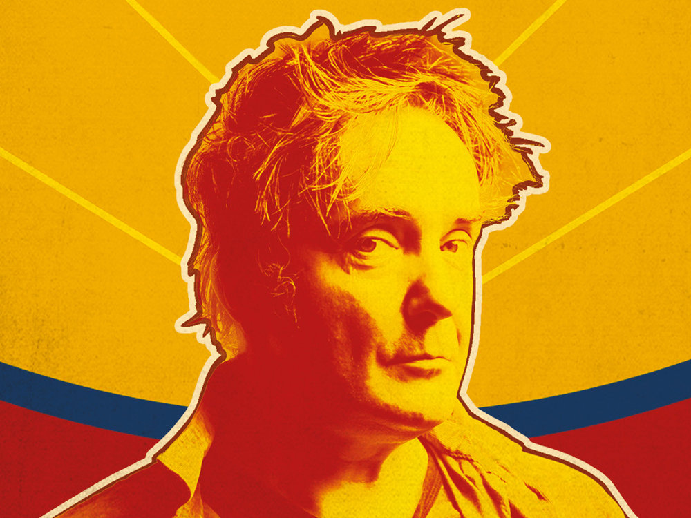 A bold, stylised portrait of a man in warm red and yellow tones, facing slightly to the side. The background features radiating yellow lines with a curved band of blue and red behind him, giving a vibrant, graphic poster-like feel.